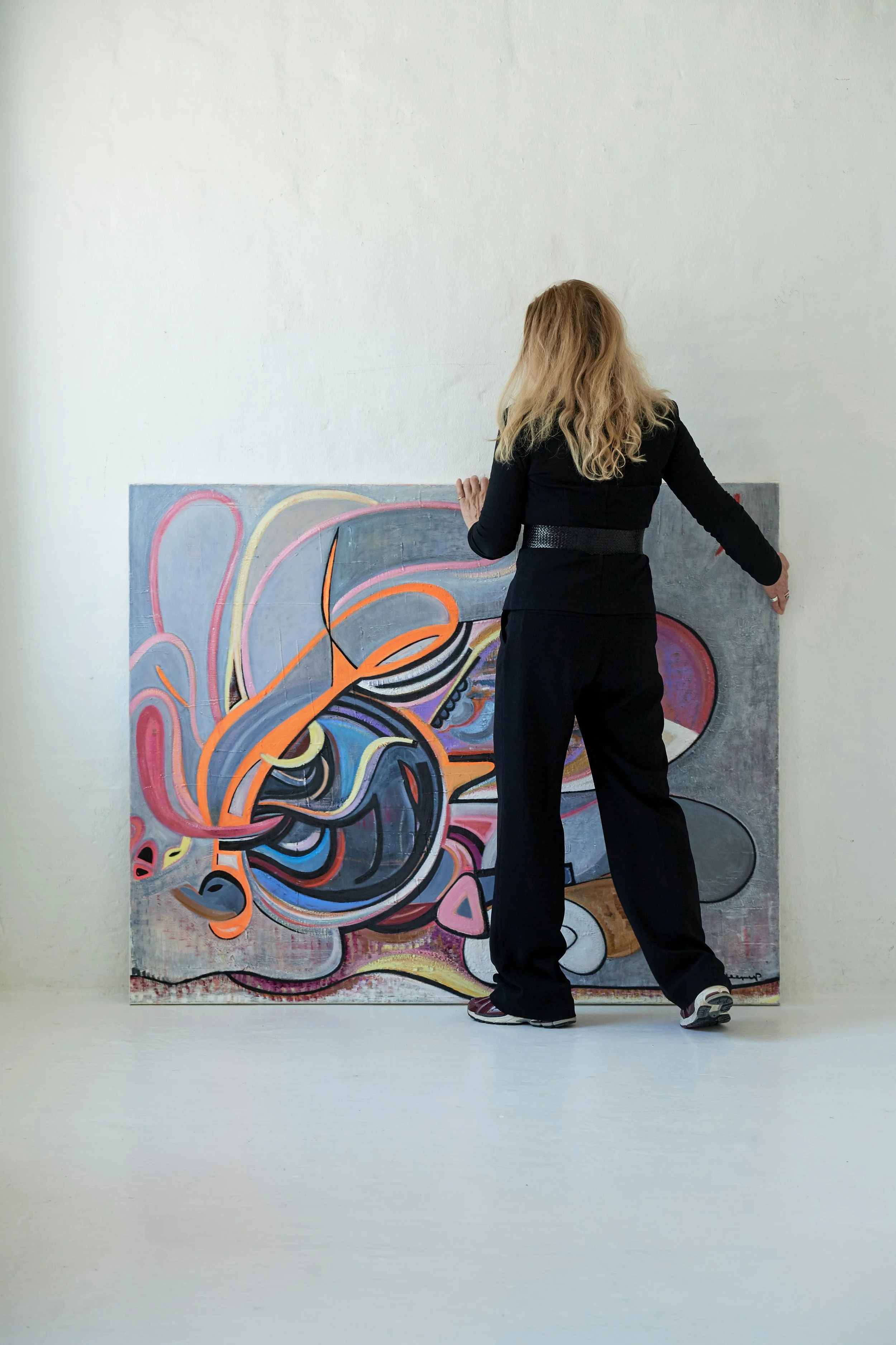 A woman in black clothing viewing colorful abstract art on a canvas.