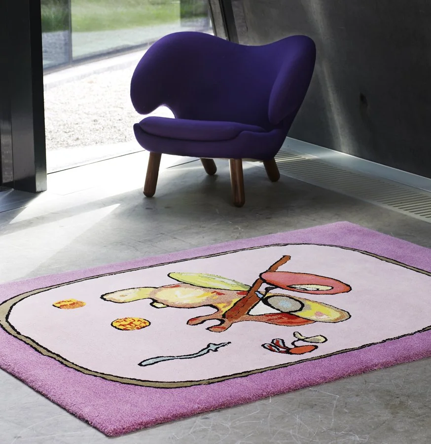 Colorful children's rug with a clock and tools design in pink, yellow, and orange, laid on a concrete floor near a purple armchair and glass door.