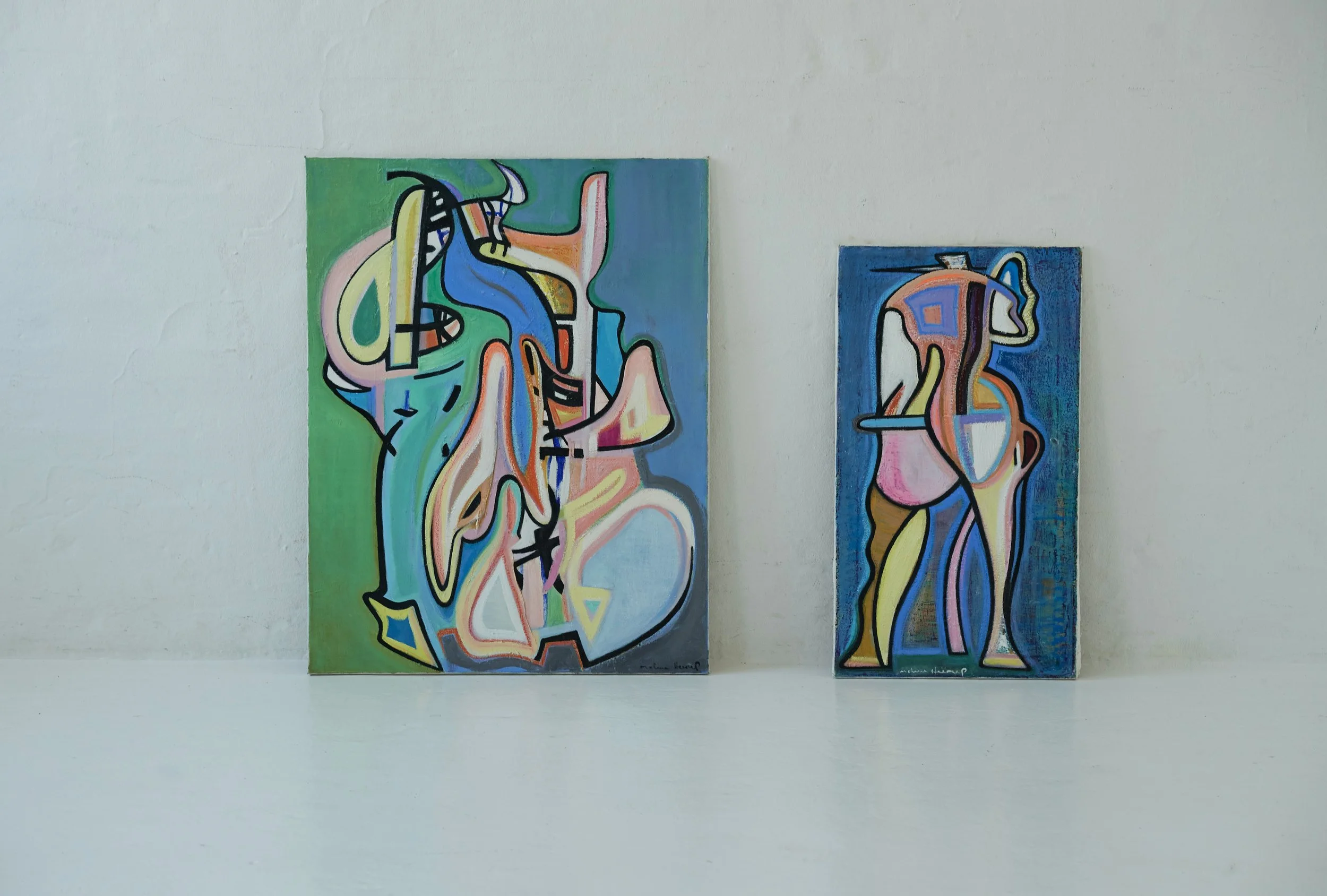 Two abstract colorful paintings on a white wall and white surface.