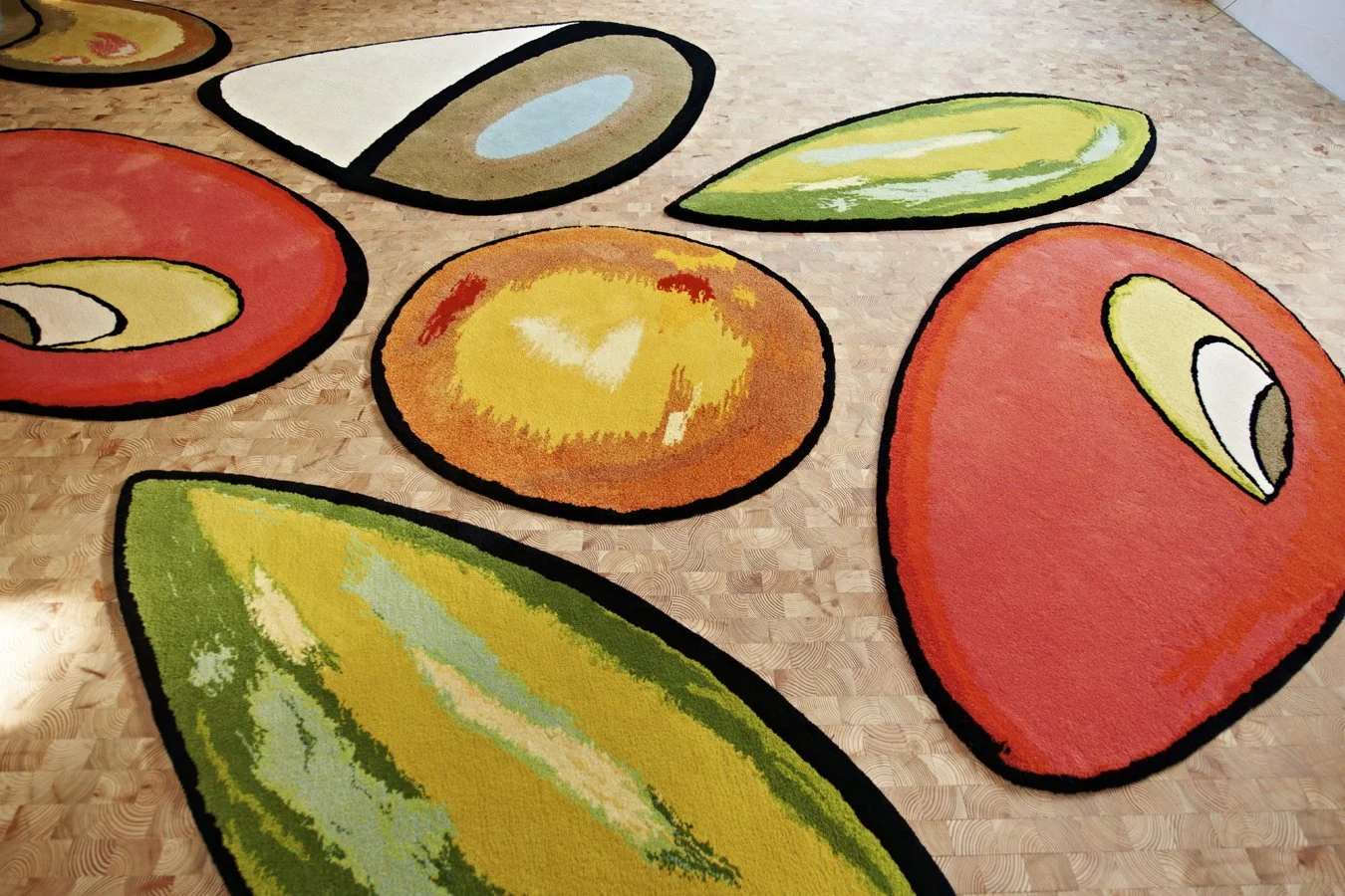 Large colorful rug with abstract fruit shapes on a wooden floor.