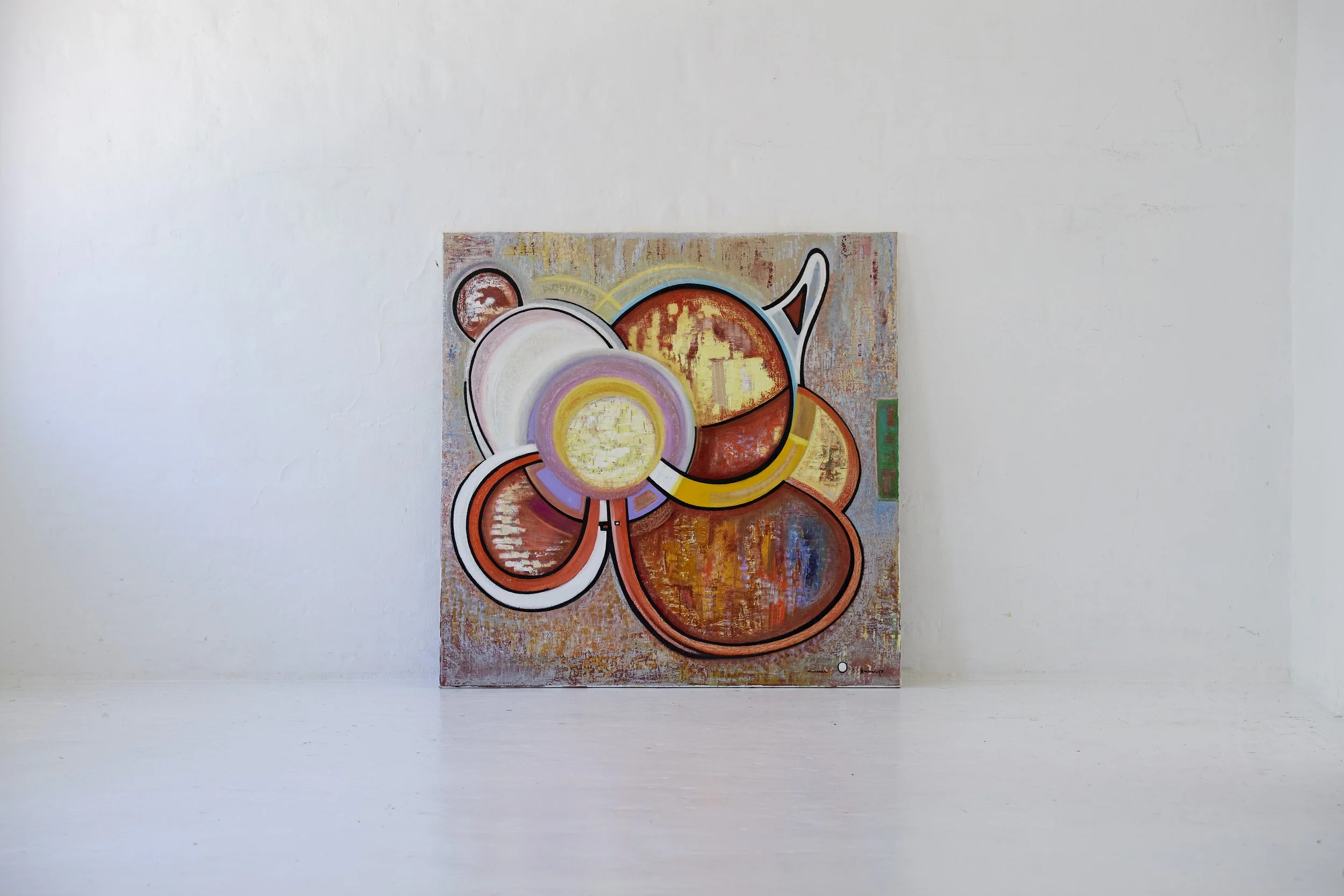 Abstract colorful painting with circular shapes on a canvas, leaning against a plain white wall.