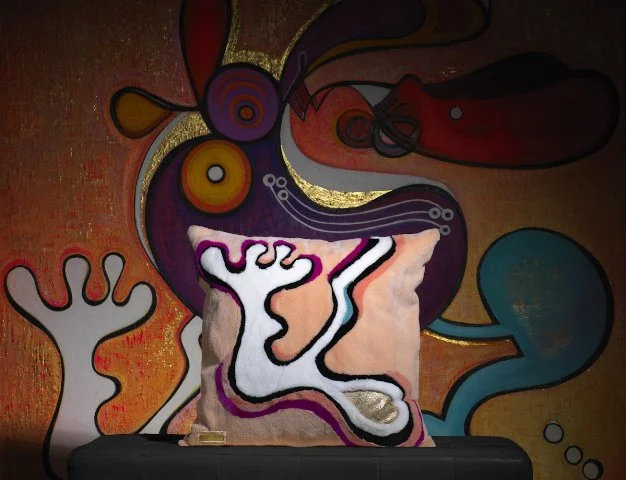 Abstract colorful wall art with shapes and lines, with a fabric pillow featuring a stylized, abstract face design in front.