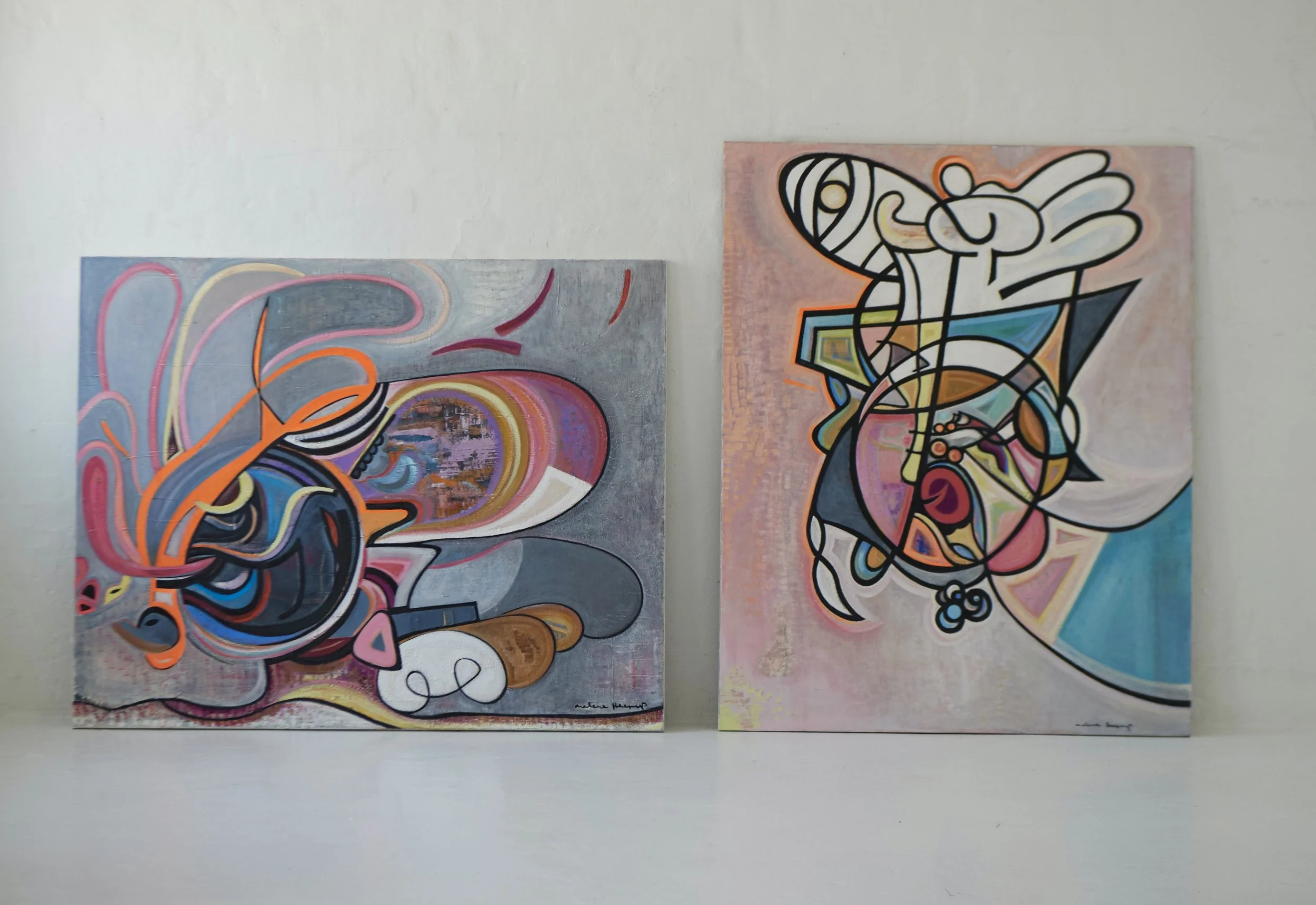 Two abstract paintings with vibrant colors and geometric shapes hanging on a white wall.