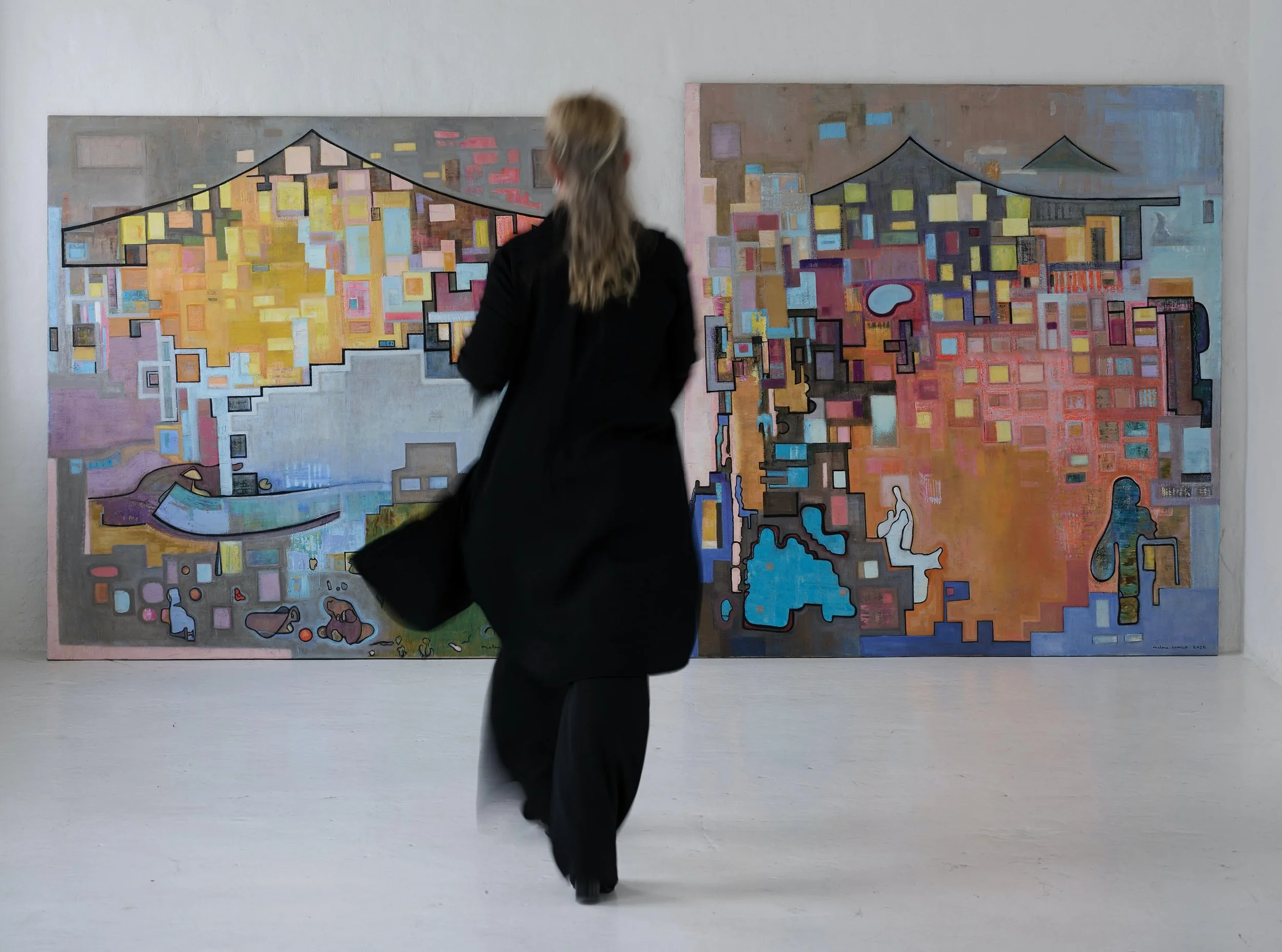 A woman with long hair, dressed in black, is walking in front of two colorful abstract paintings in an art gallery.