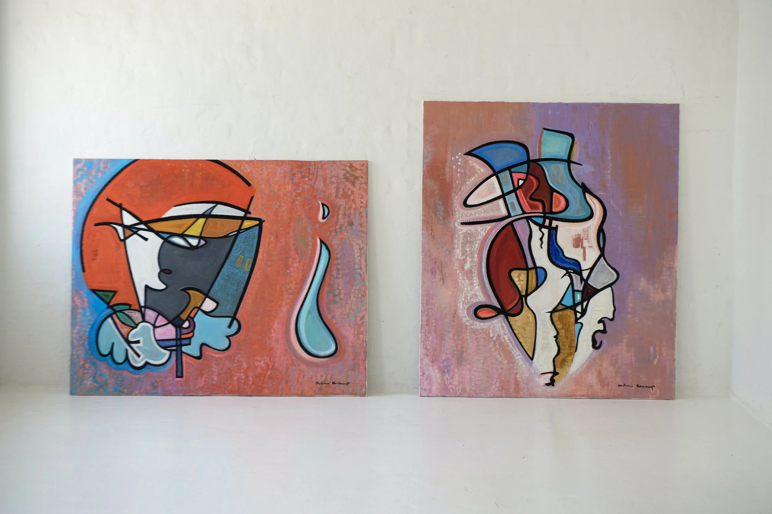 Two abstract paintings featuring stylized female faces and portraits with vibrant colors and geometric shapes, displayed on a white gallery wall.