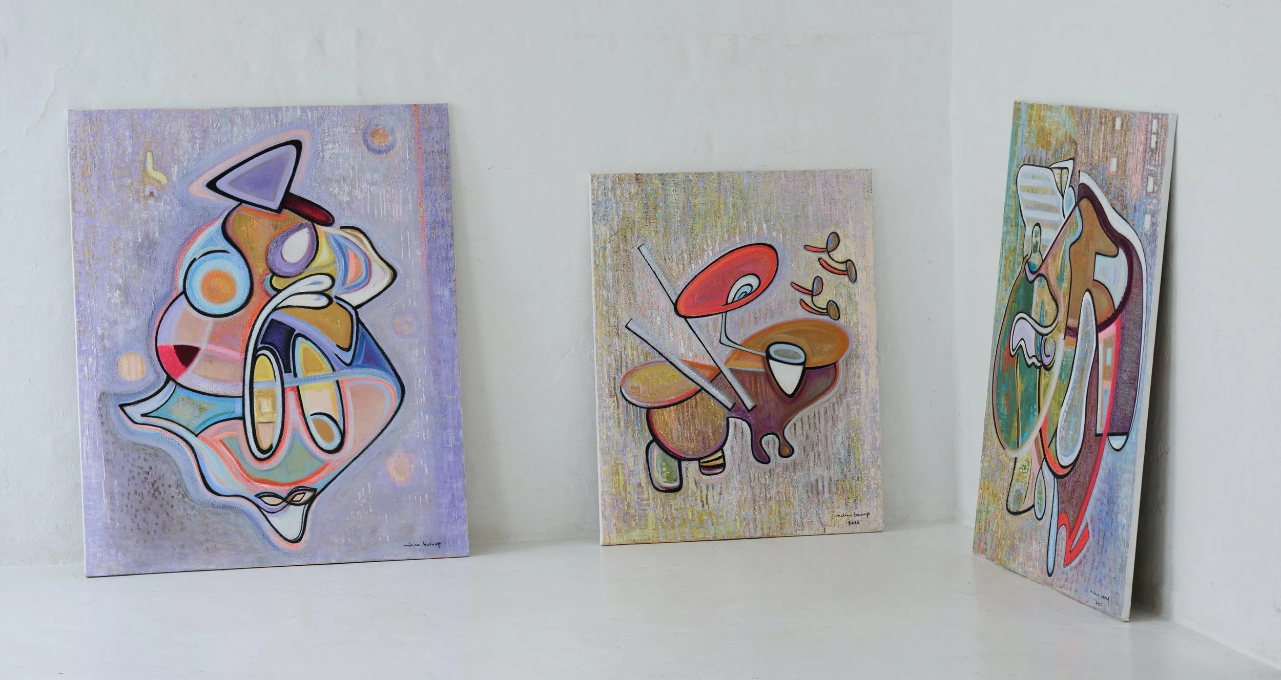 Three colorful abstract paintings leaning against a white wall.