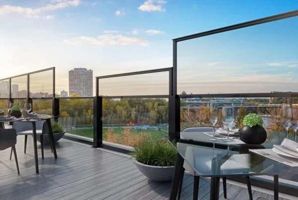 Rooftop balcony with dining tables, chairs, and a view of trees, buildings, and a bridge in the distance during dusk.