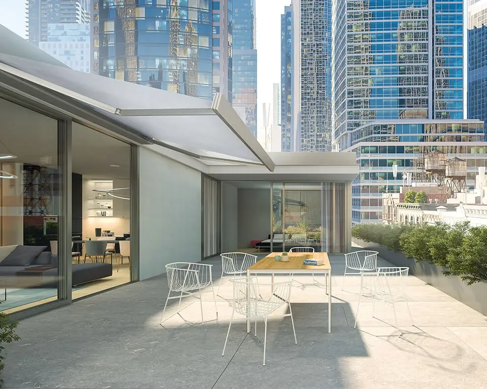 Modern outdoor terrace with a dining table and chairs, overlooking a city skyline with tall glass buildings.