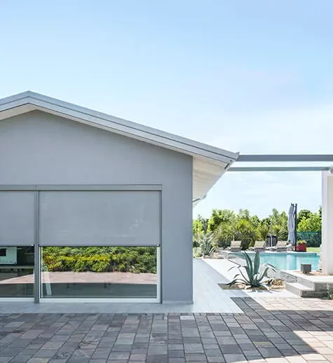 Modern house with a glass sliding door, outdoor patio with pavers, and a swimming pool surrounded by greenery.