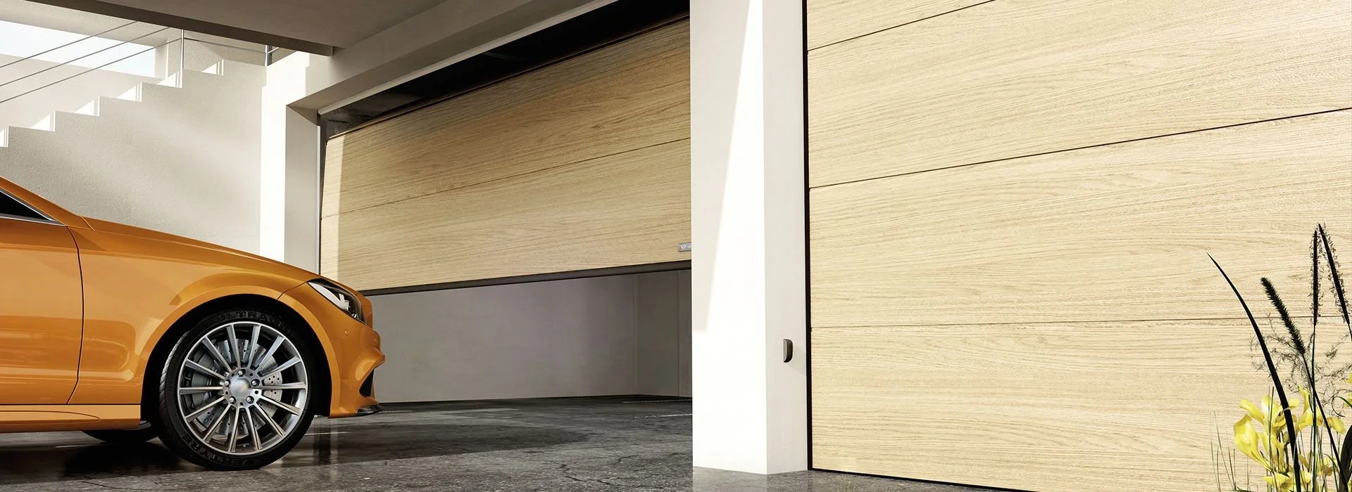 Part of an orange car with a black tire and alloy wheel is parked indoors in front of a beige wooden wall with horizontal panels. There is a white staircase with a glass railing above and to the left, and some plants are visible on the right.