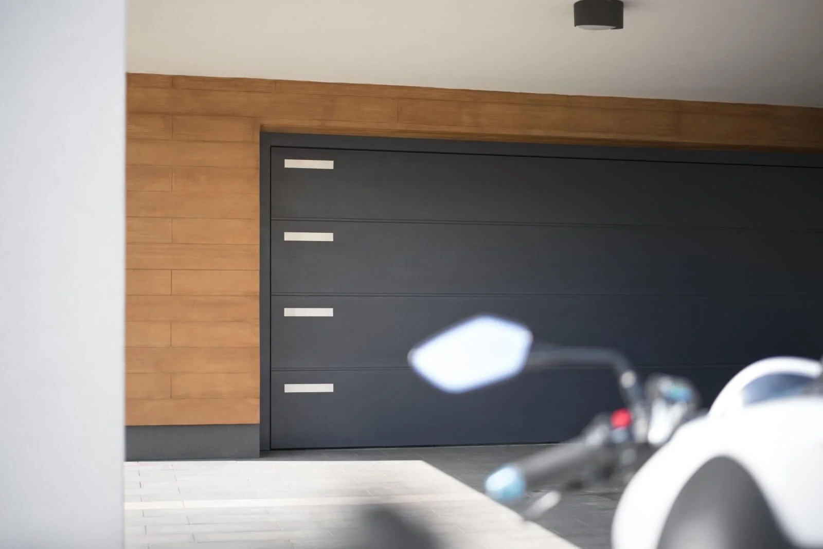 A modern garage door with a black panel design and horizontal silver handles, framed by a wooden wall in a contemporary interior.