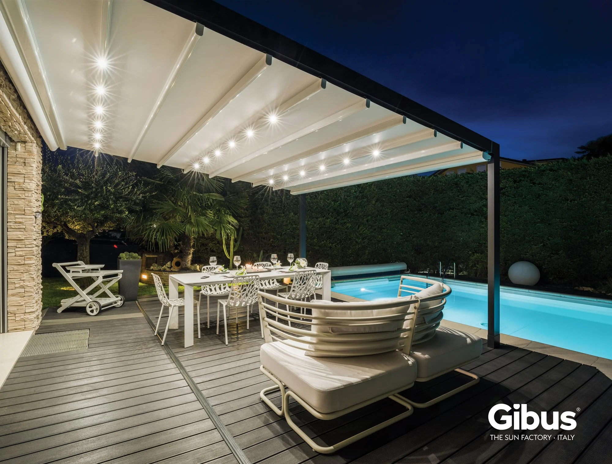 Outdoor patio at night with a dining table, chairs, lounge chairs, a swimming pool, and a covered area with lighting.