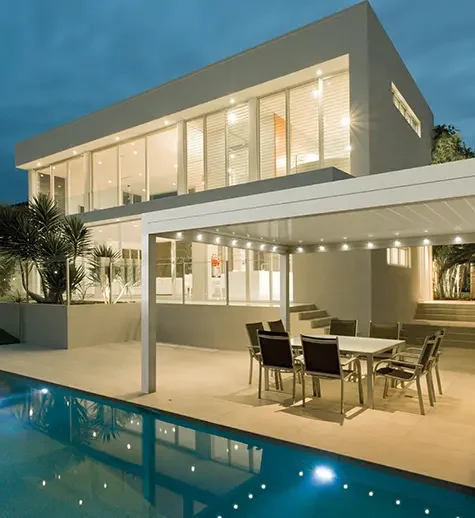 Modern two-story house with large glass windows and a swimming pool outside, illuminated at night.