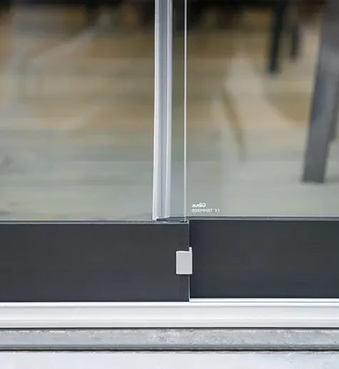 Close-up of a sliding glass door with metal frame and track, showing the bottom part of the door and the floor.
