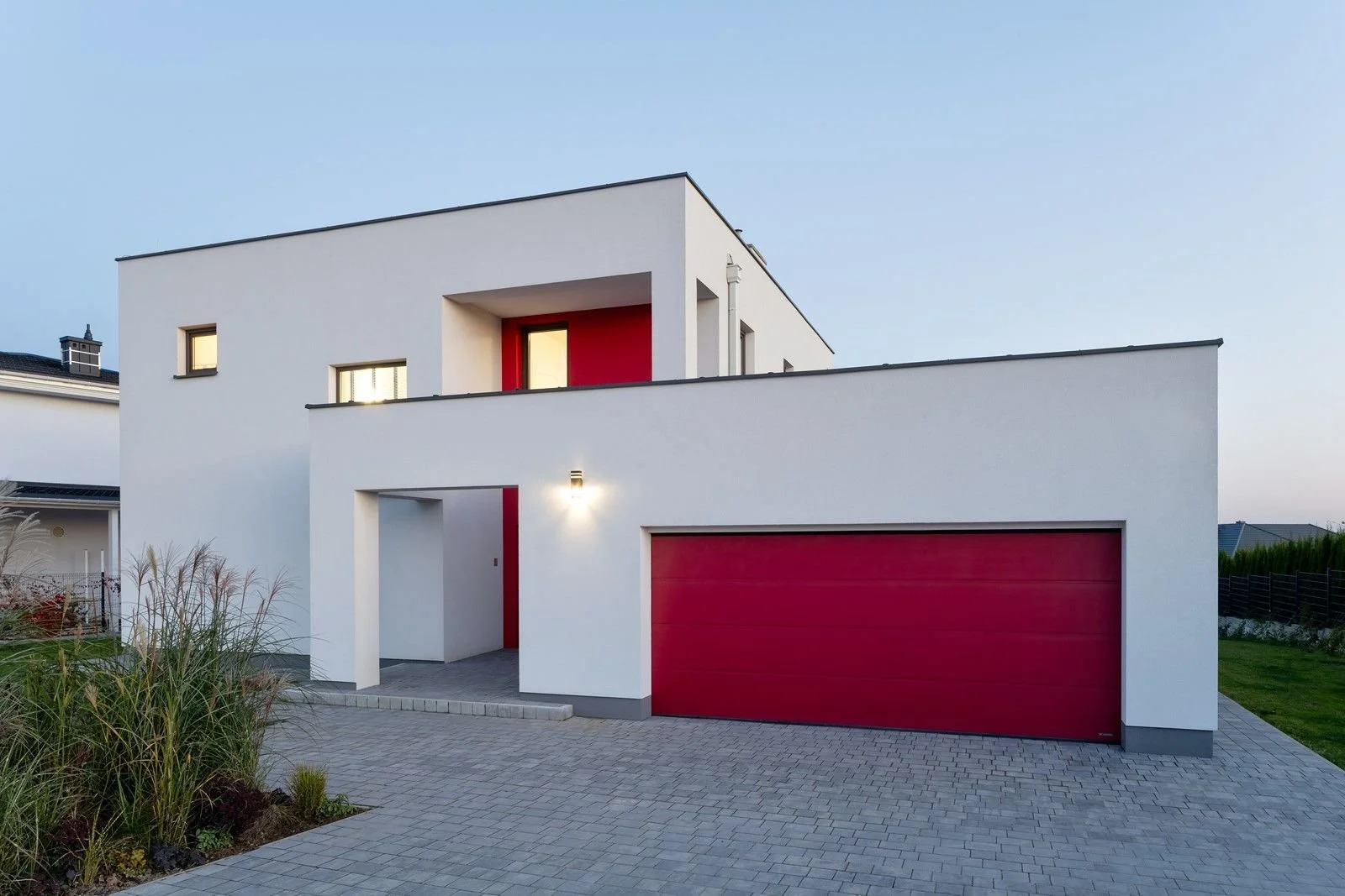 Modern two-story house with a white exterior, red garage door, and red accent wall near the entrance, with a paved driveway and minimal landscaping.