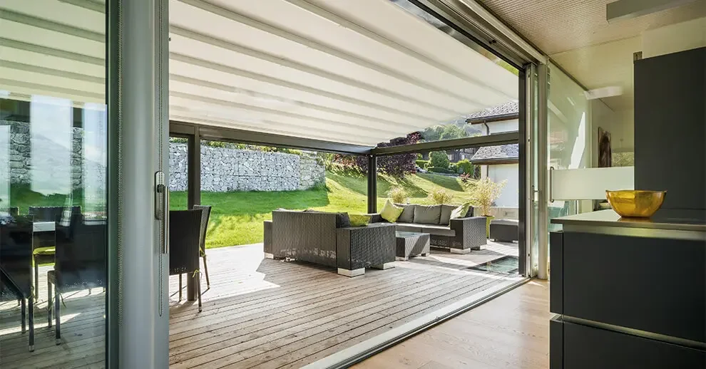 Interior view of a modern home with an open sliding glass door leading to a patio with outdoor seating, overlooking a green lawn and garden.