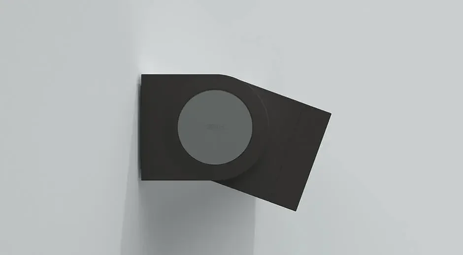 A black cylindrical speaker mounted on a white wall.