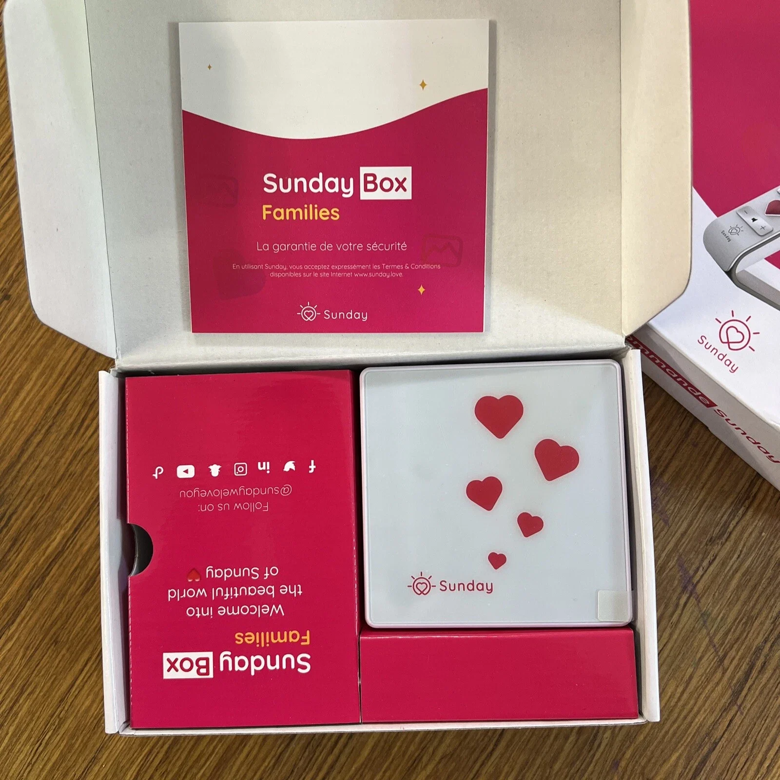 Une boîte contenant une carte avec des cœurs rouges, un panneau avec le logo de Sunday et des textes promotionnels, et une fiche d'information sur la sécurité pour une box familiale Sunday.