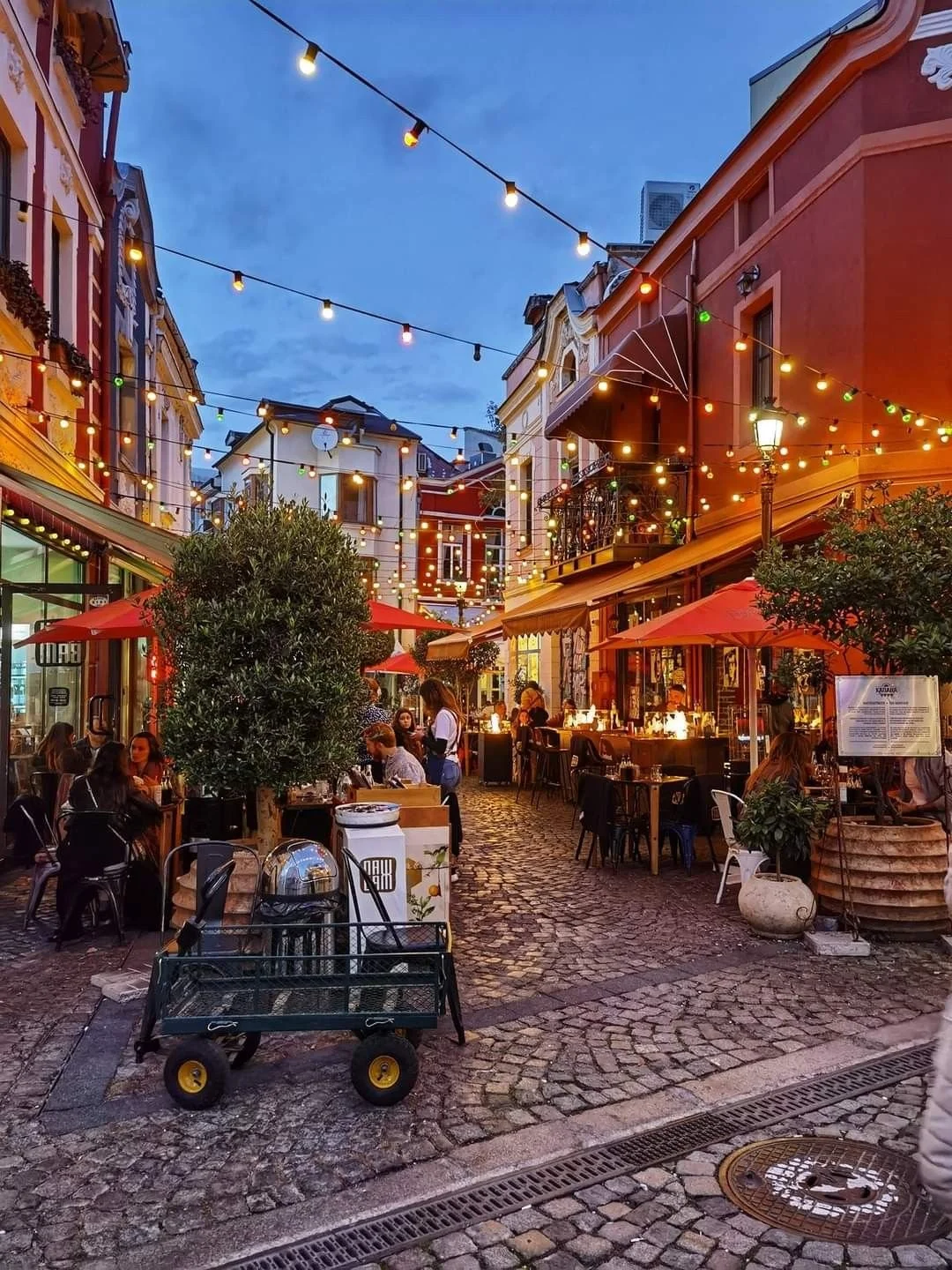 Rue animée en Bulgarie avec cafés en plein air, ambiance chaleureuse et locale au crépuscule