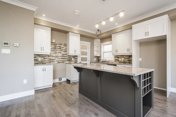 Modern kitchen with white cabinets, a black island, and a beige backsplash. Recessed and track lighting on the ceiling. Hardwood floors.