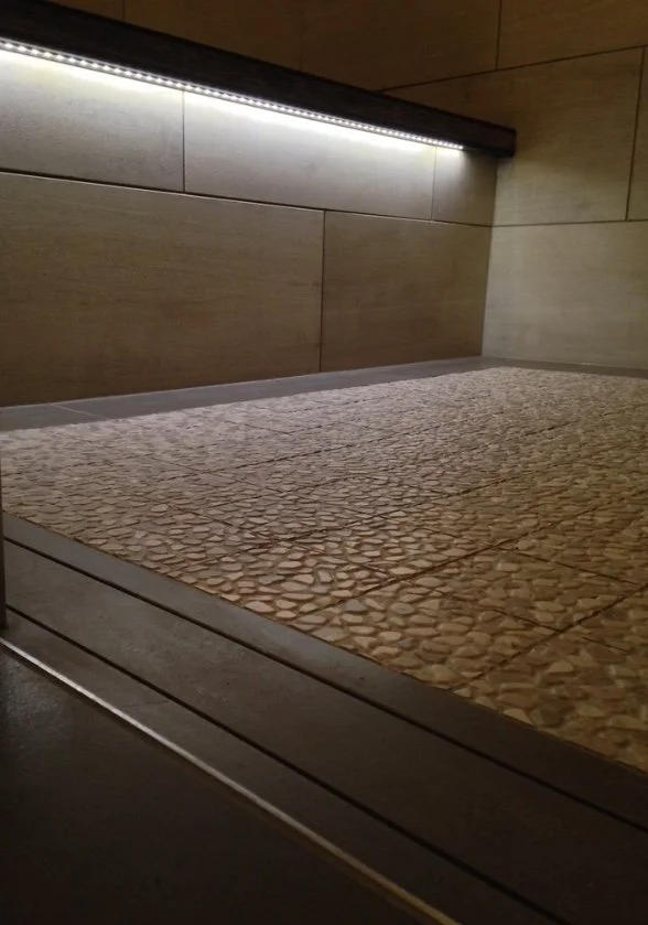 A custom shower with an LED light strip above a textured, pebble-like surfaced tile.