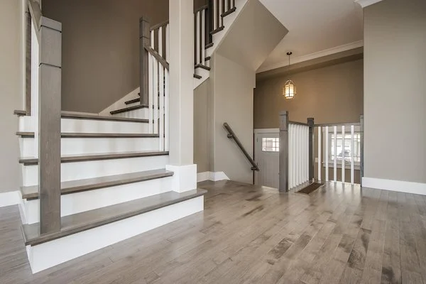 Interior of a house showing a staircase with wooden steps and gray railings, a small landing with a window, and a hanging lantern light