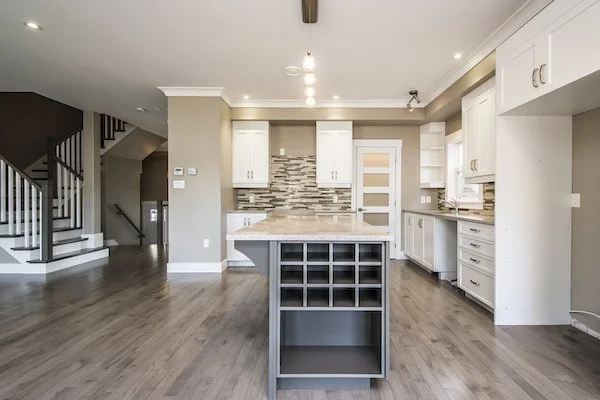 Modern kitchen with white cabinets, a tiled backsplash, and a center island with cubby storage, in an open-concept living space.
