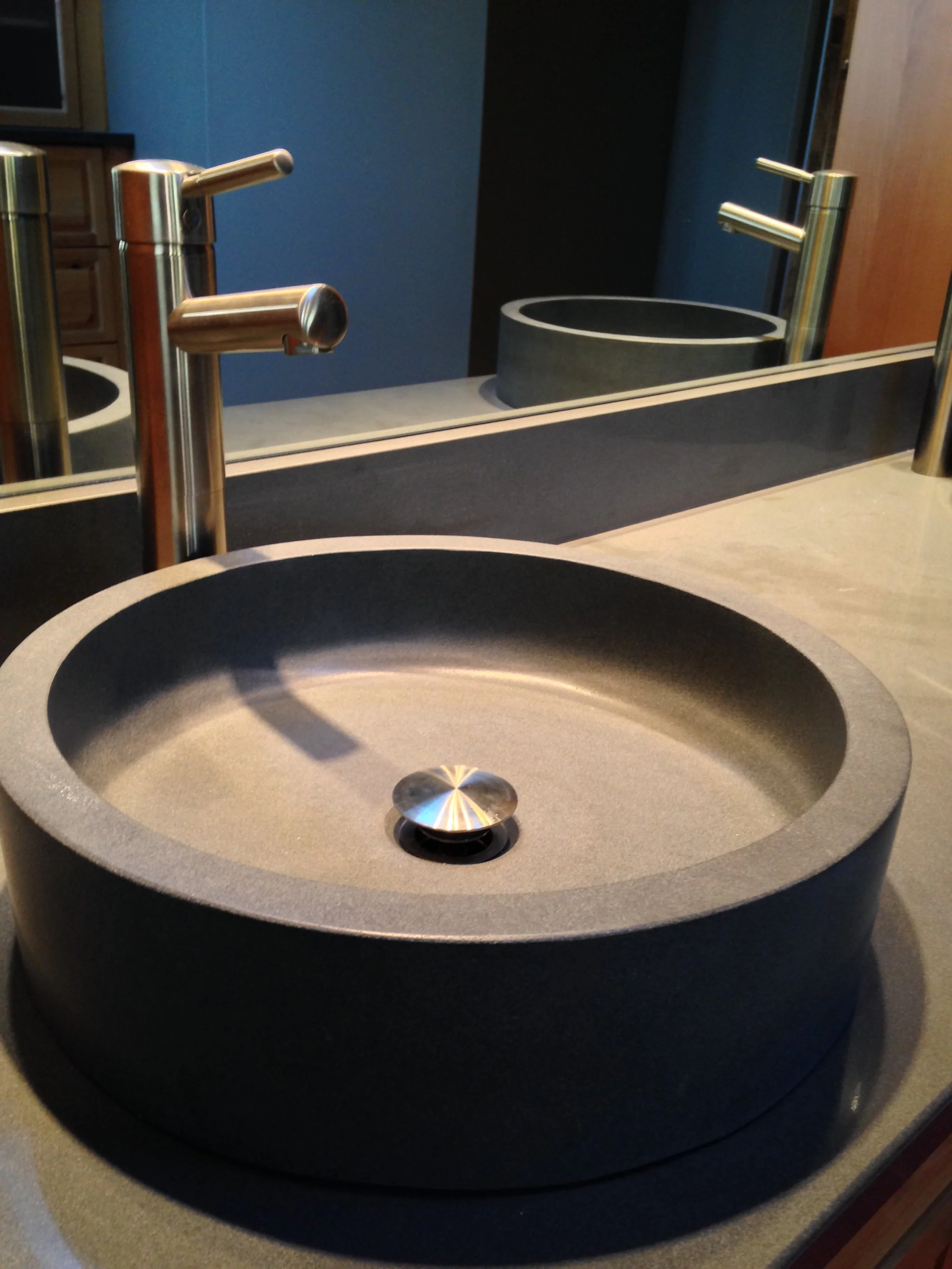 A modern bathroom sink with a black stone basin and metallic faucet, with a mirror and a second sink in the background.