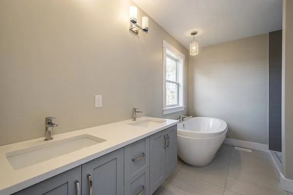 Modern bathroom with double vanity, two sinks, large round bathtub, window, and minimal decor.