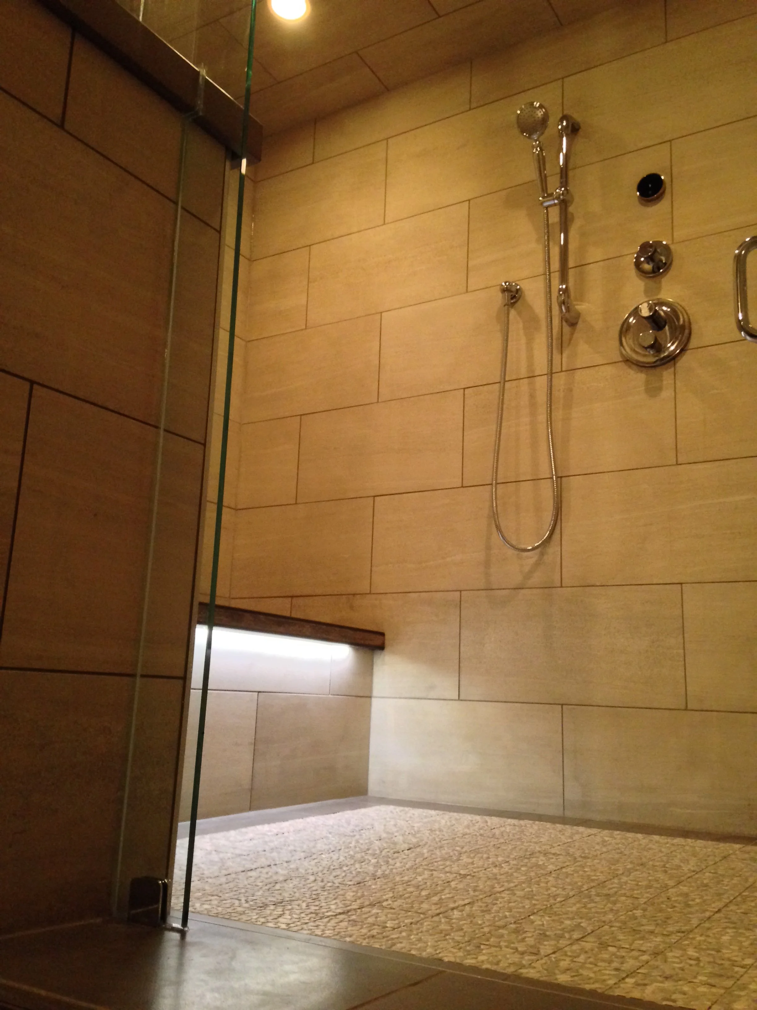 Stylish modern shower with beige tiles, a bench, and chrome fixtures.