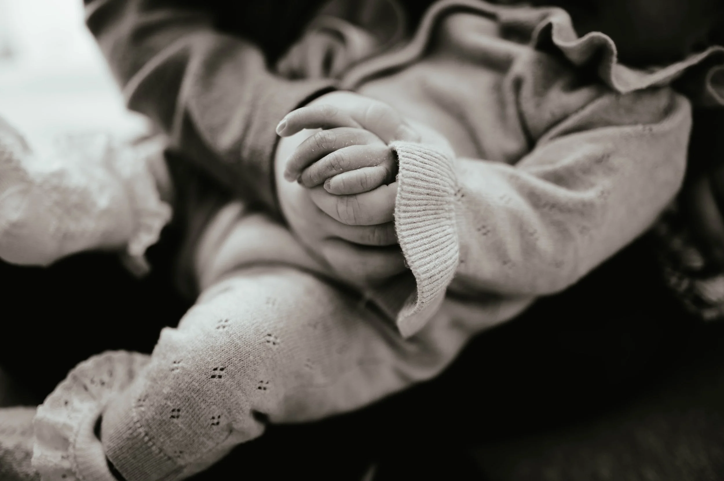 Close-up of a child's hands clasped together, wearing cozy knitted clothing in black and white.