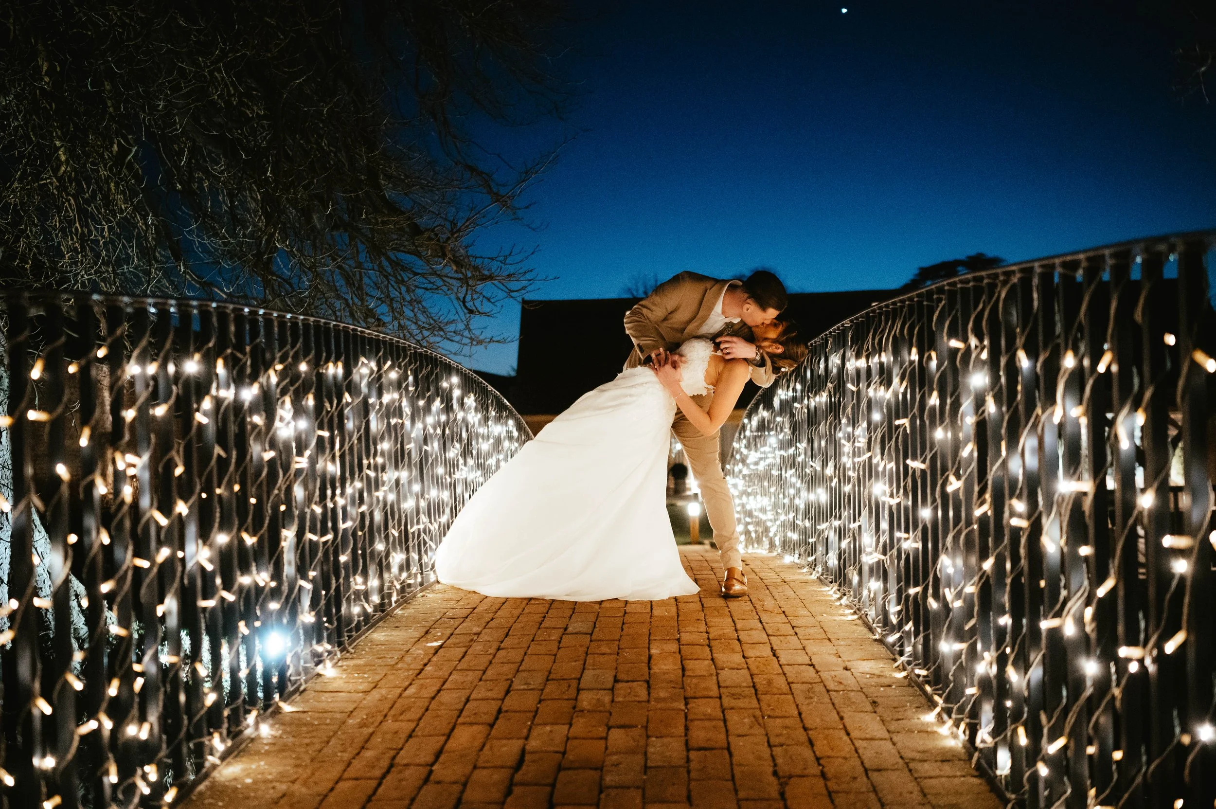 A couple sharing a romantic dance on a bridge at night, surrounded by string lights, with a dark sky overhead.