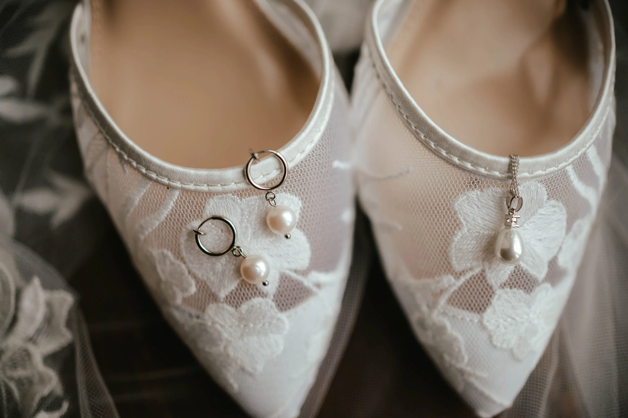 White lace bridal shoes with pearl jewelry inside, including earrings and a necklace with pearl pendant.