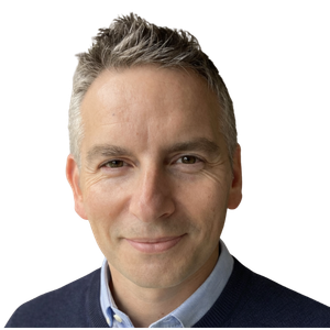 Close-up portrait of Rich Allen with gray hair, smiling slightly, wearing a blue collared shirt and navy sweater.