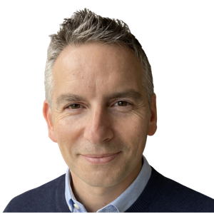 Close-up portrait of Rich Allen with gray hair, smiling slightly, wearing a blue collared shirt and navy sweater.