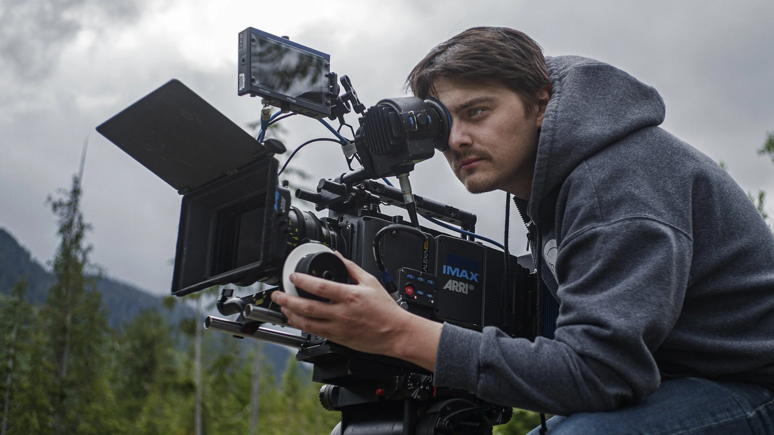 Man operating a professional video camera outdoors on a cloudy day.