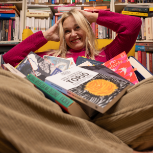 Woman smiling in a bookstore or library with books in front of her and shelves of books behind her.