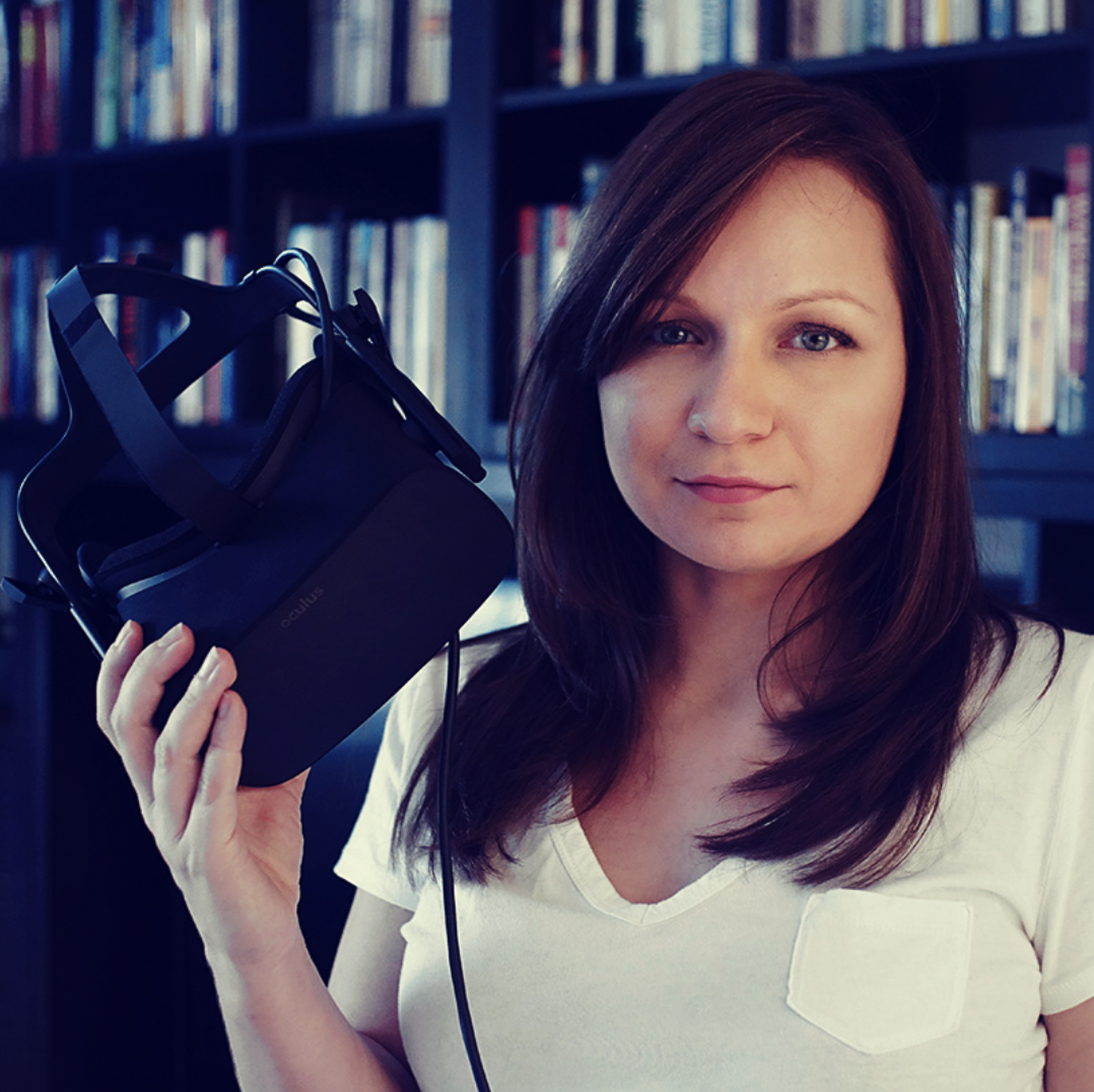 Woman holding Oculus virtual reality headset in front of bookshelves.
