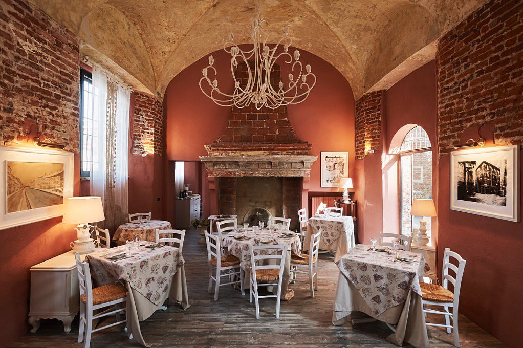 Sala ristorante in castello del XIV secolo con pareti in mattoni a vista e camino.