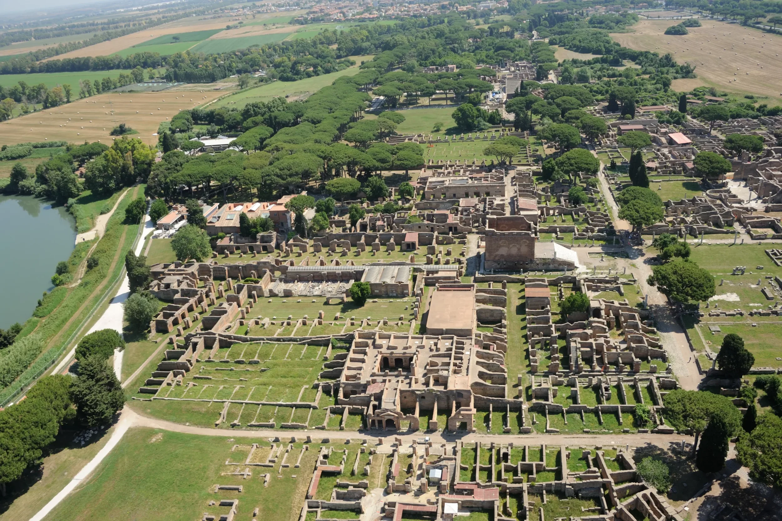 Aerial view of the ancient ruins of Pompeii, Italy, showing ruins, green trees, a nearby lake, and surrounding fields.