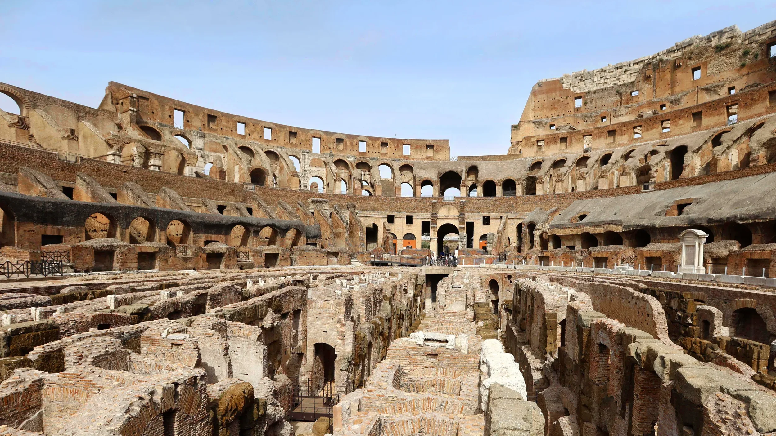 The interior of the Roman Colosseum with visible ancient stone and brick walls, arches, and remnants of the arena floor.
