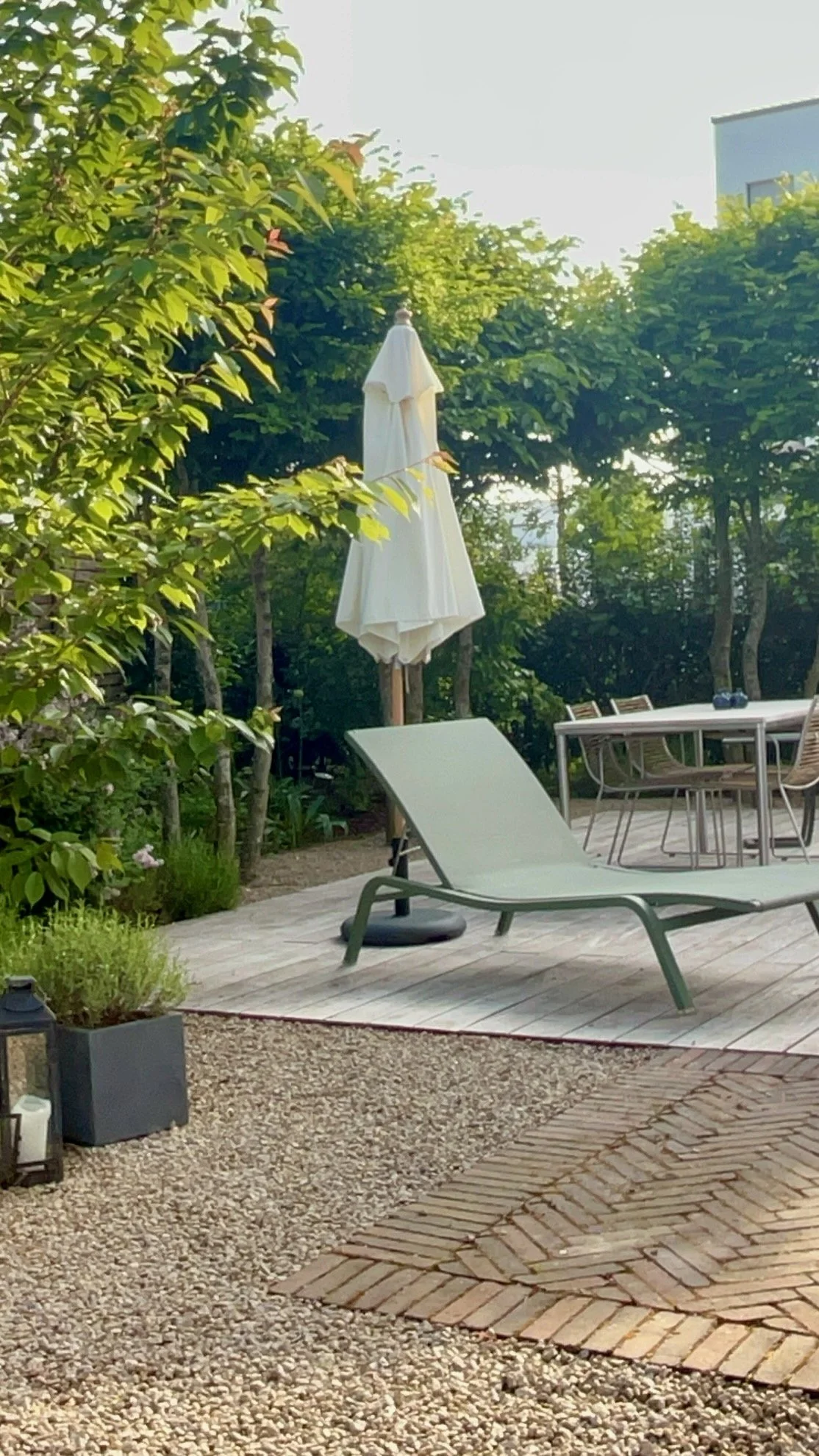 Ein Garten mit Liegestuhl, Tisch, Stühlen, geschlossenem Sonnenschirm und viel Grün.
