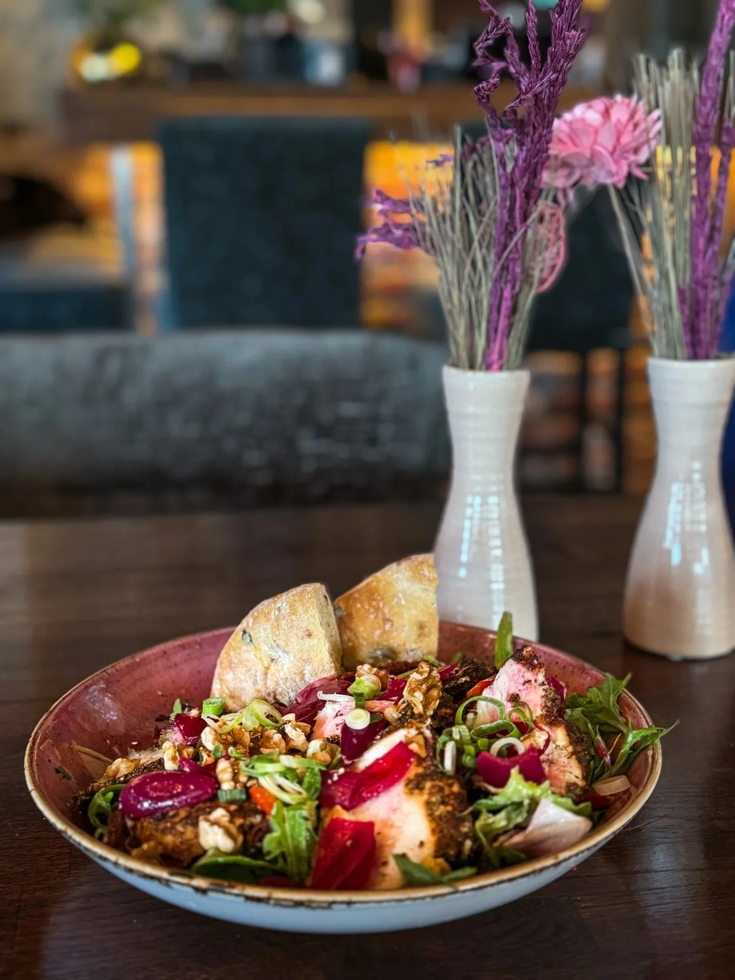 En salat med kylling, grønn løk, rødløk, granola, og brød ved siden av.