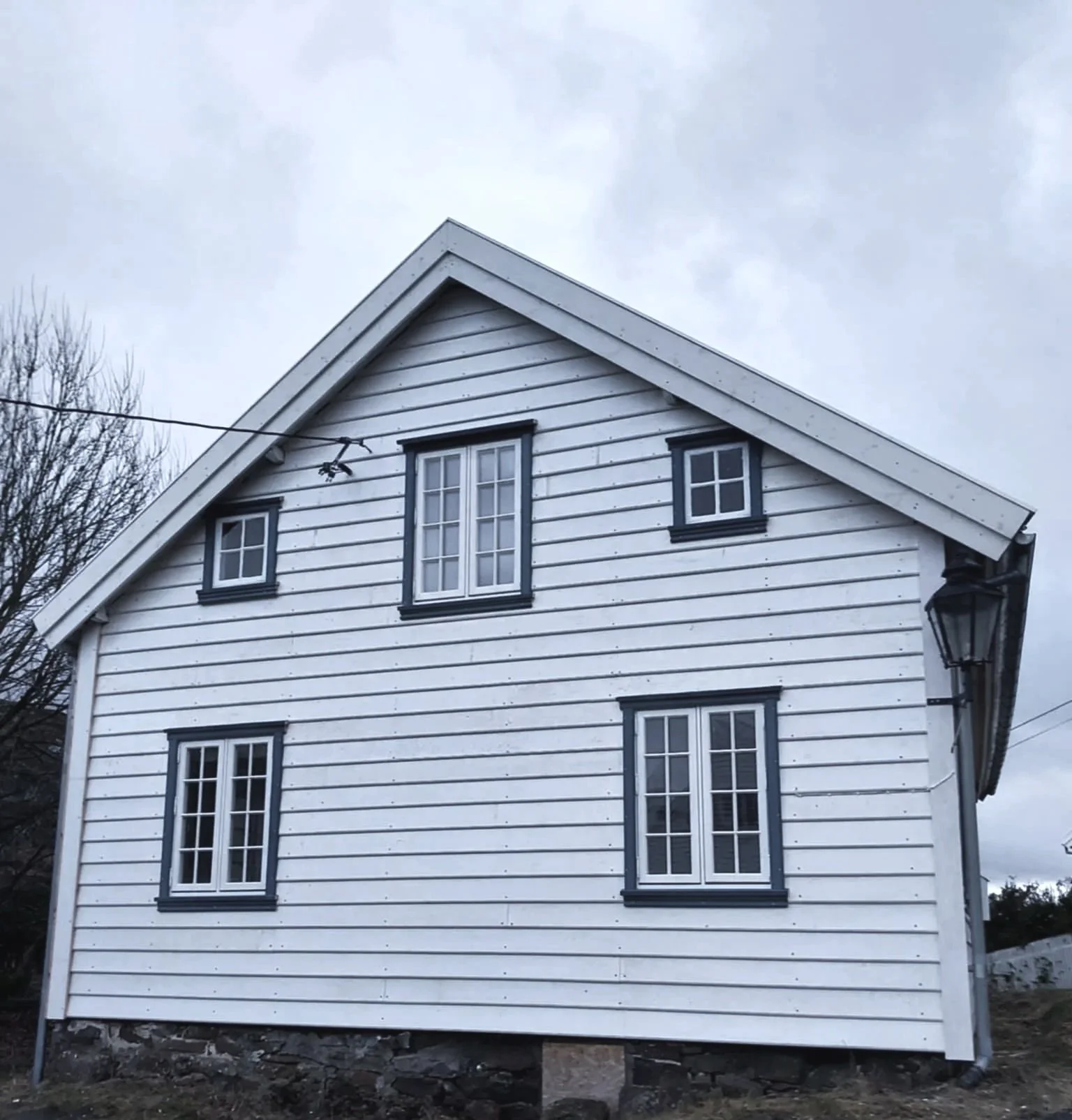Et hvitt hus med svartkantede vinduer og tre etasjer, under en mørk sky.