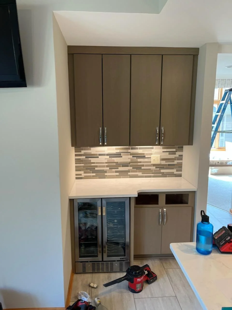 Small wet bar area with upper and lower cabinets, tile backsplash, mini wine fridge, and countertop.