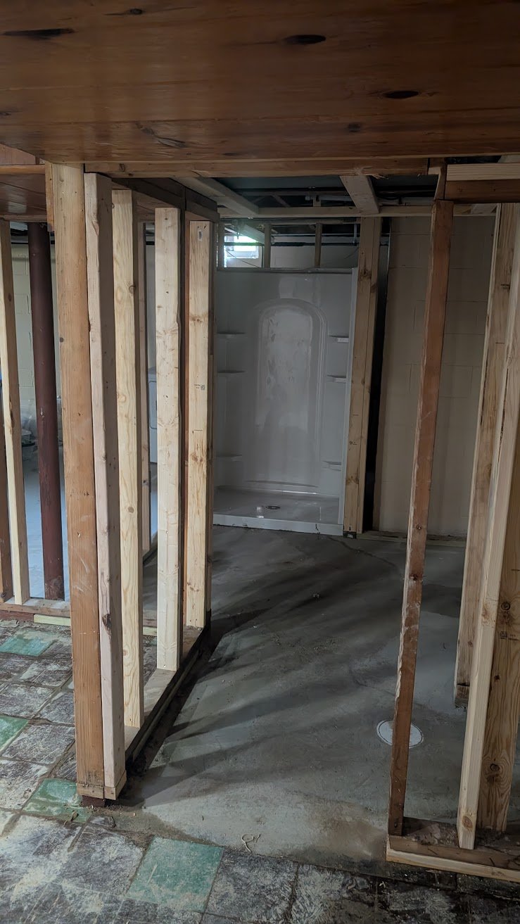 Bathroom under renovation with exposed wooden framing, a shower stall, and a concrete floor.