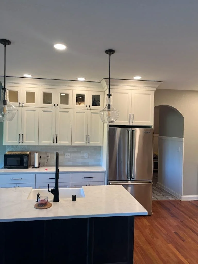 Modern kitchen with white cabinets, stainless steel refrigerator, black faucet, and a kitchen island with a candle, a small container, and a paper towel holder.