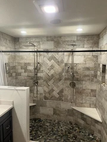 Walk-in shower with two showerheads, tiled walls, pebble tile floor, and built-in shelves in bathroom.