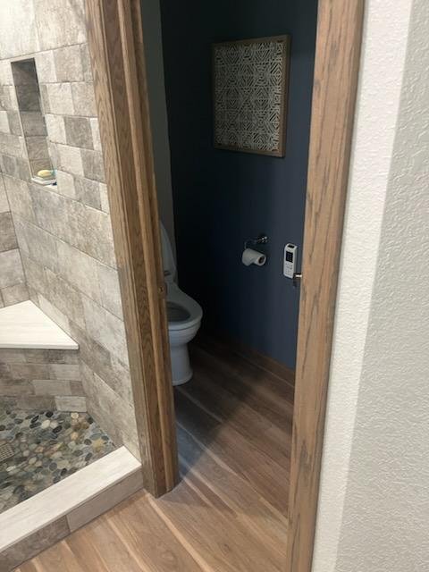 Small bathroom with toilet, navy blue wall, wood trim, framed artwork, and a remote control on the wall.