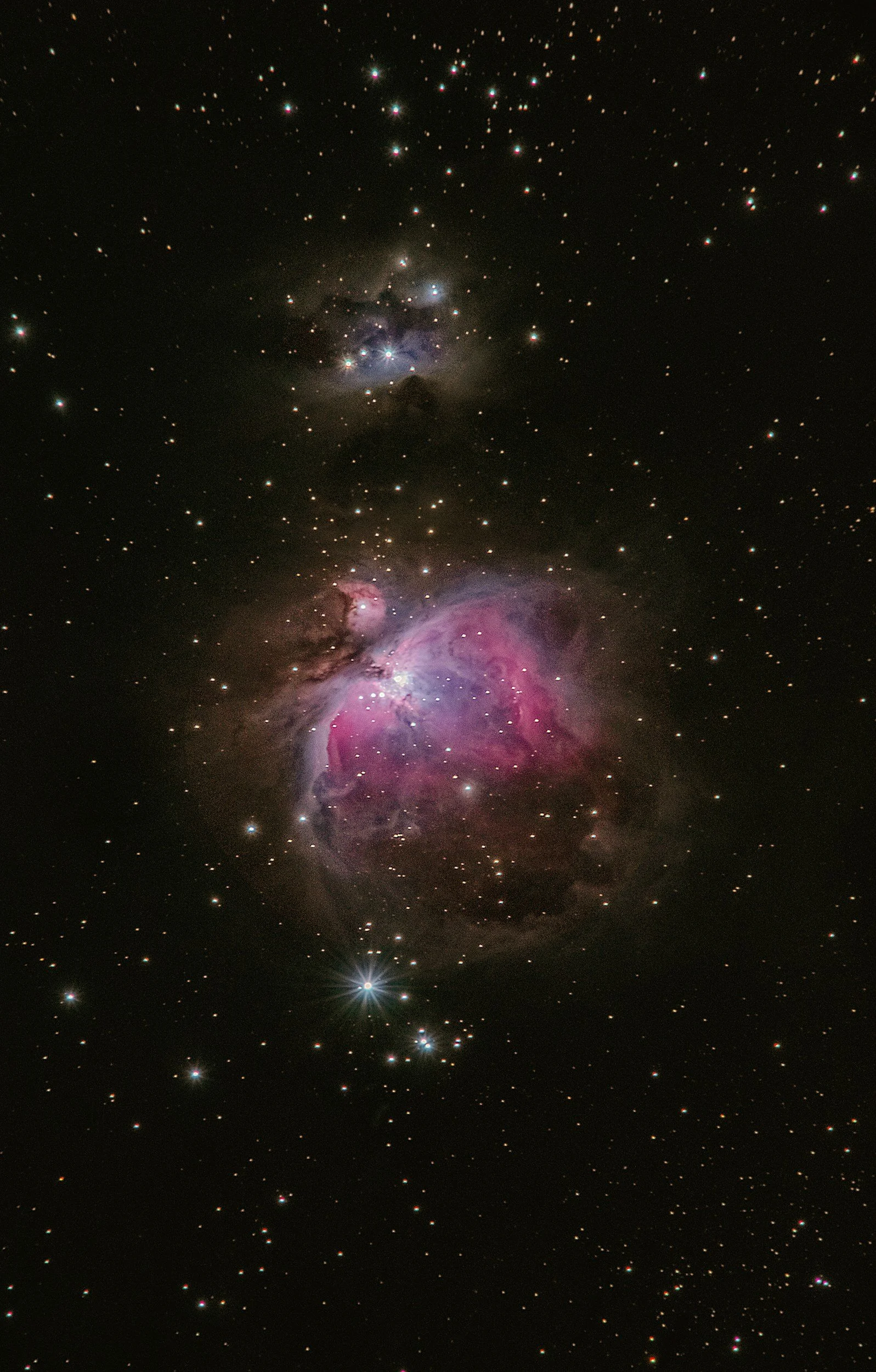 A detailed image of space showing multiple stars, nebulae, and galaxies, with a large pink and purple nebula in the center surrounded by smaller bright objects.